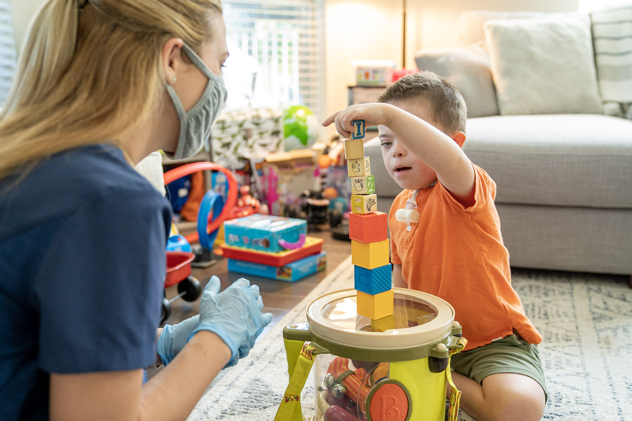 Little boy with special needs plays blocks at home with his occupational therapist.